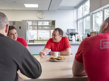 A group of firefighters laugh and chat around a table in the canteen
