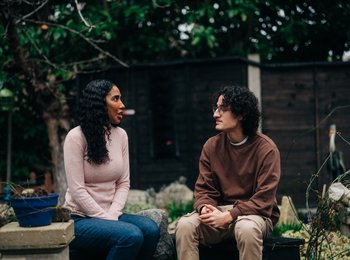 Two men sitting on a bench outside talking