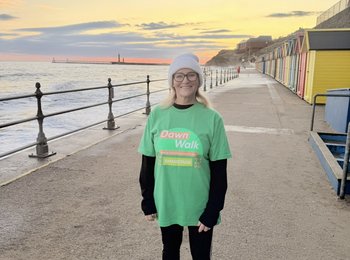 Someone wearing a Dawn Walk t-shirt doing a walk as the sun comes up at the beach