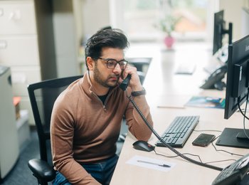 A man is sitting at a desk on the phone