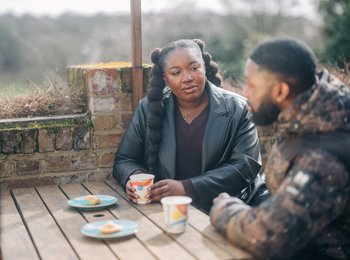 Two people sat outside talking on a bench