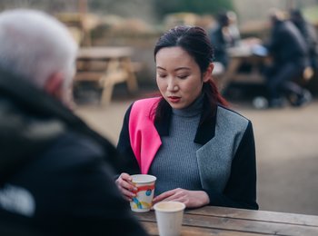 A woman sitting at a table outside talking to a man