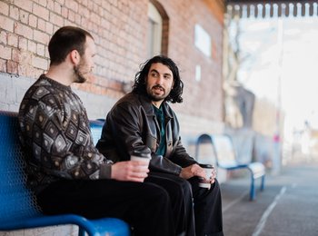 Two people sat at a train station talking